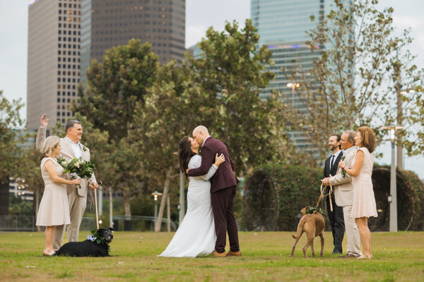 Couple kissing with Houston Skyline in the background with their parents and dogs beside them
