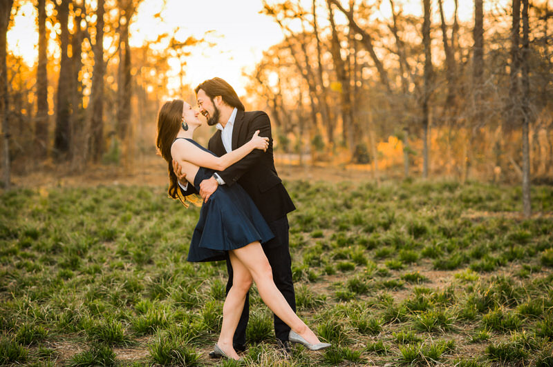 Couple in a low grass field with sunset behind them holding and looking at each other by Houston Wedding Photographers & Videographers Nate Messarra Photography