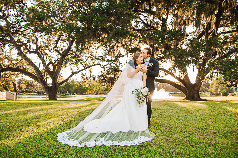 Bride and groom holding each other with sunset and oak trees in the background at Houston Oaks Wedding