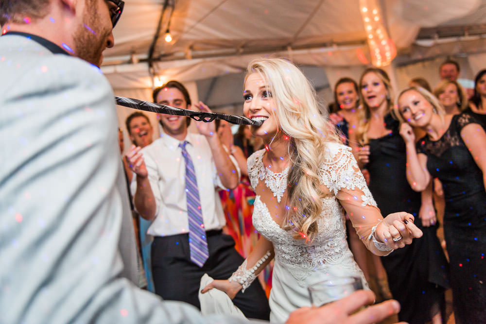 Bride with Grooms tie in her mouth on dance floor of Colorado wedding