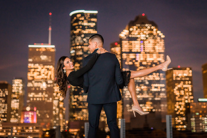 Woman in the arms of a man with the golden Houston skyline in the backdrop by Nate Messarra Photography
